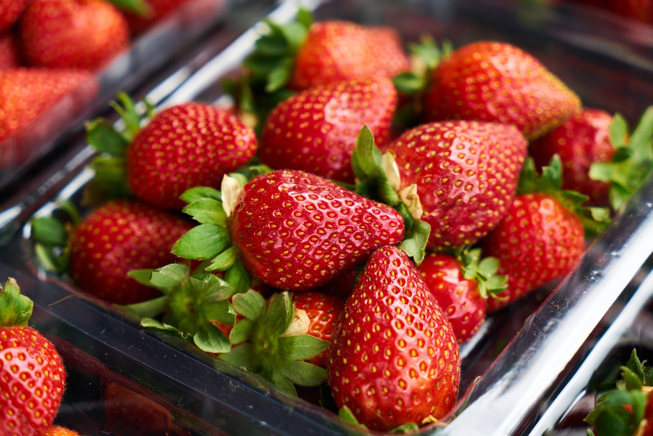 Close-up of ripe strawberries in a clear plastic container, showcasing vibrant freshness and juicy appeal.
